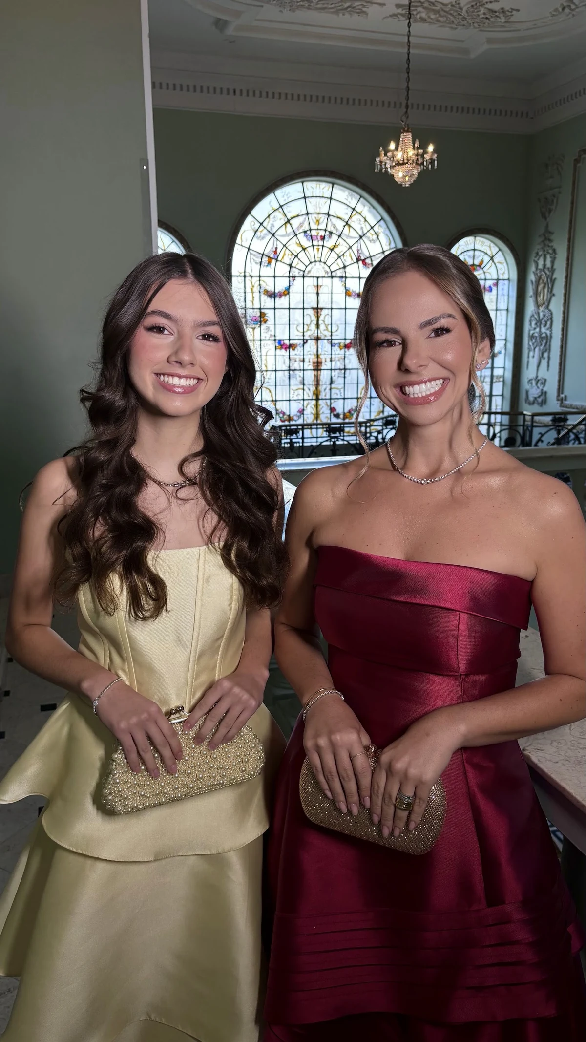 Duas mulheres com maquiagem para evento e vestidos amarelo e vinho.