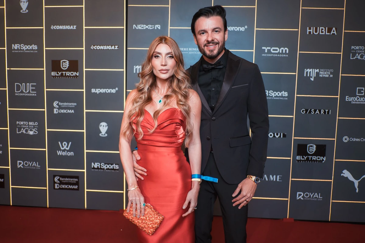 Casal em traje de festa, com vestido vermelho e roupa formal preta.