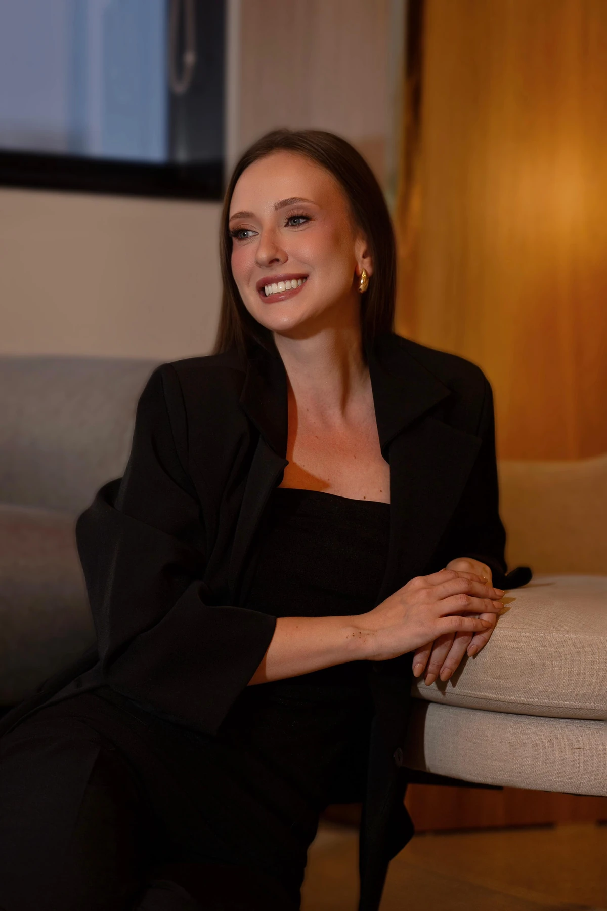Retrato profissional de mulher com blazer preto, sentada à mesa.